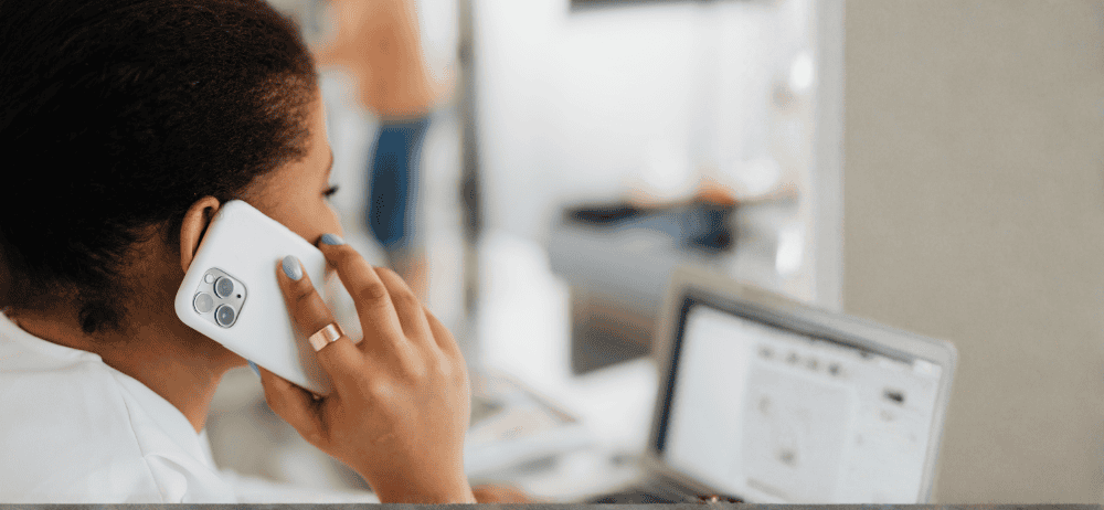 Person making a phone call, holding phone to ear. Sitting in a room with open laptop