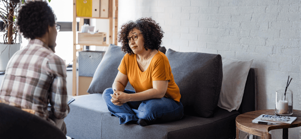 Therapist sitting with client while client sits crisscross on the couch. 