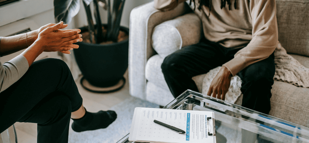 Therapist sitting with client. Therapist has hands clapped together