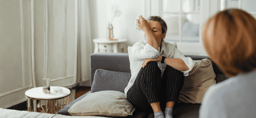 Therapist sitting with woman client who is in distress clutching tissue and covering face.